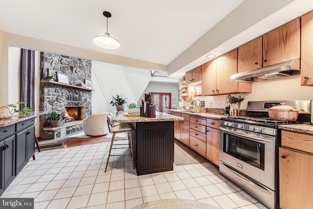 kitchen featuring stainless steel gas range oven, hanging light fixtures, light stone counters, a kitchen breakfast bar, and a center island