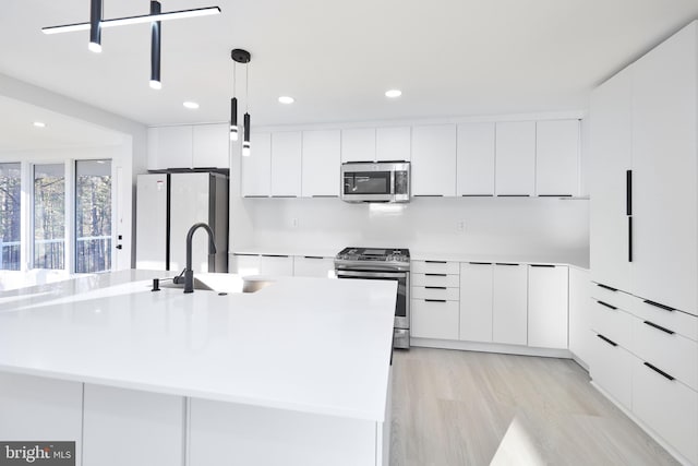 kitchen with sink, stainless steel appliances, pendant lighting, and an island with sink