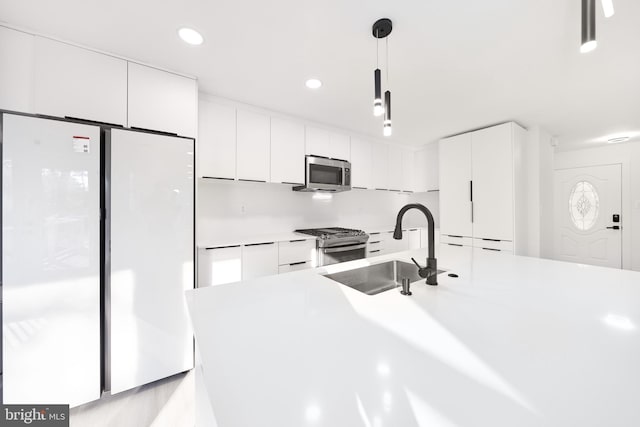 kitchen featuring stainless steel appliances, pendant lighting, white cabinetry, and sink