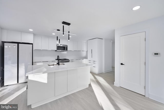 kitchen featuring white cabinetry, appliances with stainless steel finishes, a kitchen island with sink, hanging light fixtures, and sink