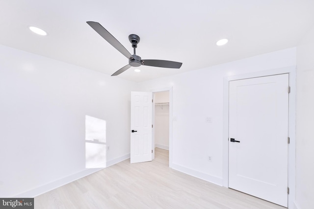 unfurnished bedroom featuring ceiling fan, a spacious closet, a closet, and light wood-type flooring