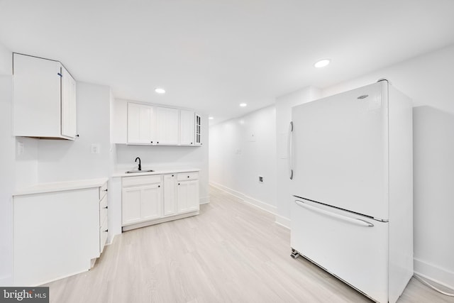 kitchen with light hardwood / wood-style flooring, sink, white fridge, and white cabinetry