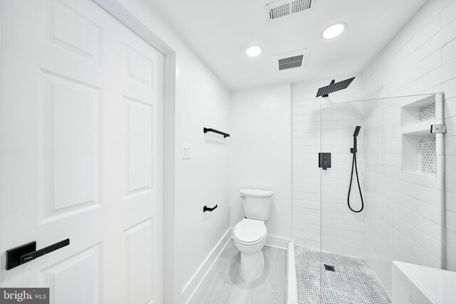 bathroom with toilet, a tile shower, and hardwood / wood-style floors