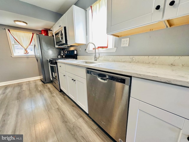 kitchen with light stone countertops, white cabinetry, light wood-type flooring, and appliances with stainless steel finishes