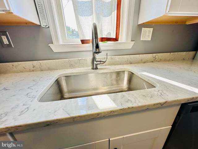 interior details featuring white cabinets, dishwasher, light stone countertops, and sink