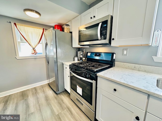 kitchen with light stone countertops, light wood-type flooring, white cabinetry, and stainless steel appliances