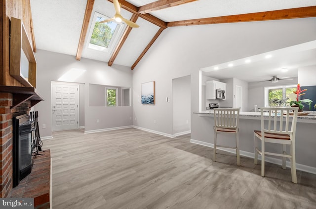 living room with a fireplace, light hardwood / wood-style floors, a skylight, and ceiling fan