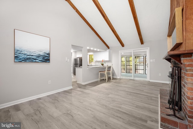 living room with high vaulted ceiling, a fireplace, light hardwood / wood-style floors, and beamed ceiling