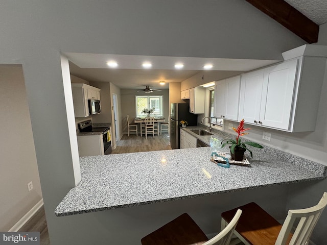 kitchen with stainless steel appliances, white cabinets, sink, kitchen peninsula, and a breakfast bar area