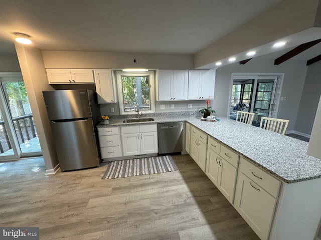 kitchen with light stone counters, sink, kitchen peninsula, appliances with stainless steel finishes, and light wood-type flooring