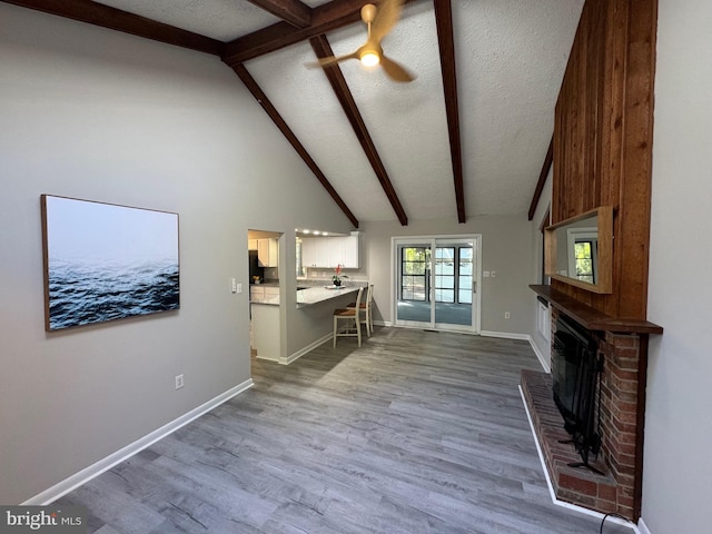 unfurnished living room with light wood-type flooring, beamed ceiling, ceiling fan, high vaulted ceiling, and a textured ceiling