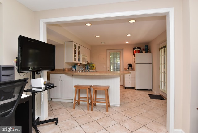 kitchen featuring light tile patterned flooring, white appliances, a breakfast bar area, kitchen peninsula, and white cabinets