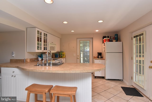 kitchen featuring a kitchen breakfast bar, kitchen peninsula, white appliances, and white cabinetry