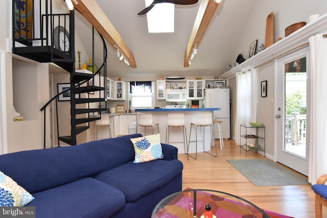 living room featuring ceiling fan, vaulted ceiling with beams, and light wood-type flooring