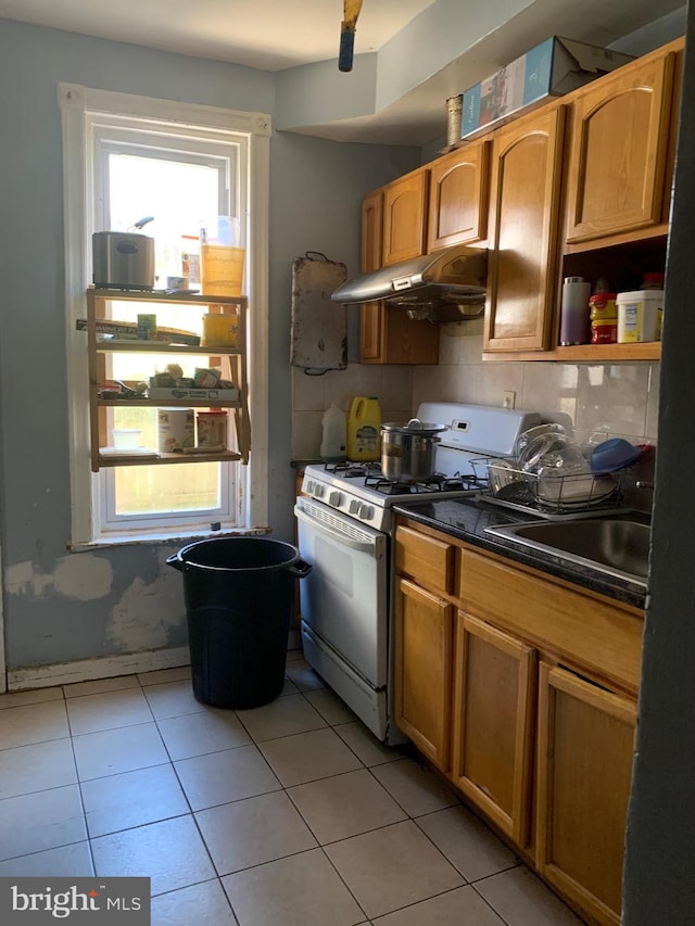 kitchen featuring light tile patterned flooring, white gas range oven, and sink