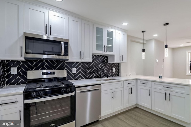 kitchen with white cabinets, a sink, light wood-type flooring, stainless steel appliances, and backsplash