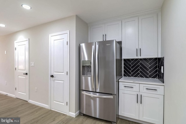 kitchen featuring stainless steel fridge with ice dispenser, white cabinets, light countertops, and backsplash