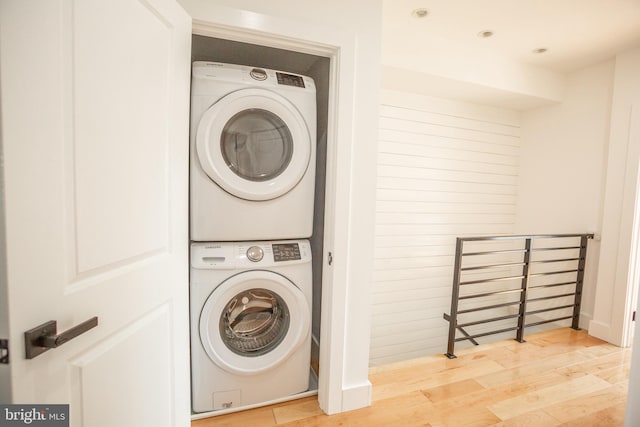 laundry area with stacked washer and dryer and light wood-type flooring