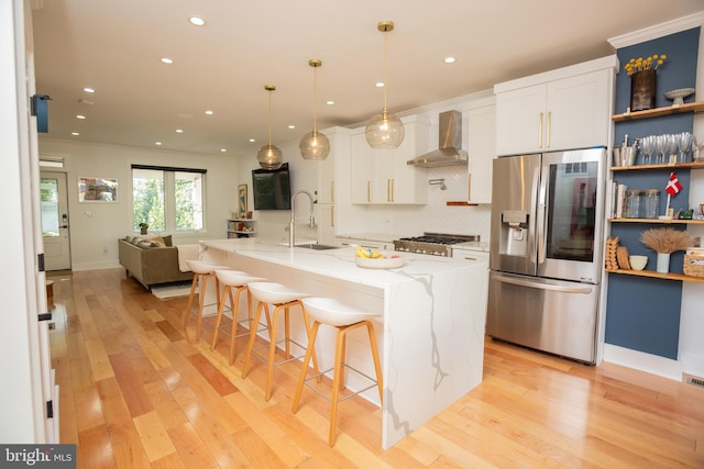 kitchen with wall chimney exhaust hood, light wood-type flooring, pendant lighting, stainless steel appliances, and white cabinetry