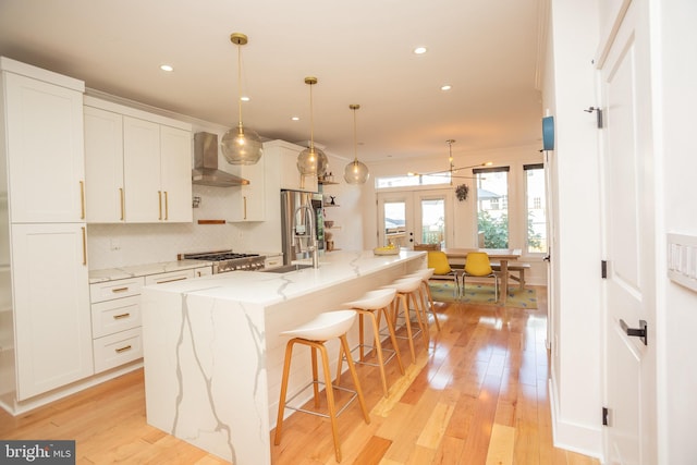 kitchen featuring pendant lighting, a large island with sink, light wood-type flooring, and white cabinetry