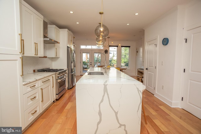 kitchen with an island with sink, light wood-type flooring, white cabinets, appliances with stainless steel finishes, and decorative light fixtures