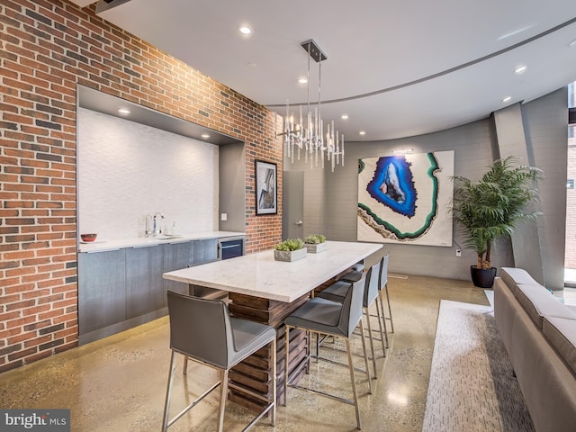 dining space with a notable chandelier, brick wall, and sink