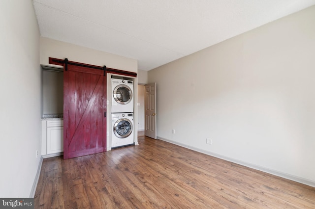 laundry area featuring stacked washer / dryer, a barn door, and wood-type flooring