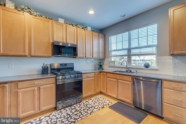 kitchen with stainless steel appliances, tasteful backsplash, sink, and light wood-type flooring