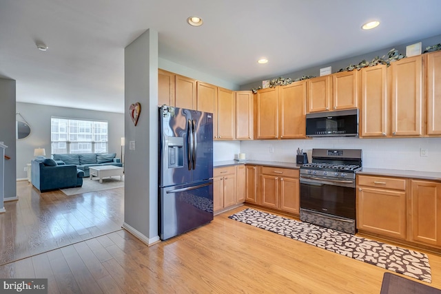 kitchen featuring decorative backsplash, light brown cabinets, range with gas stovetop, black refrigerator with ice dispenser, and light hardwood / wood-style floors