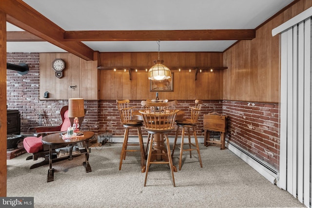 dining space with beamed ceiling, wood walls, brick wall, baseboard heating, and light colored carpet