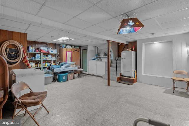 basement featuring a paneled ceiling, washing machine and clothes dryer, carpet flooring, and wooden walls