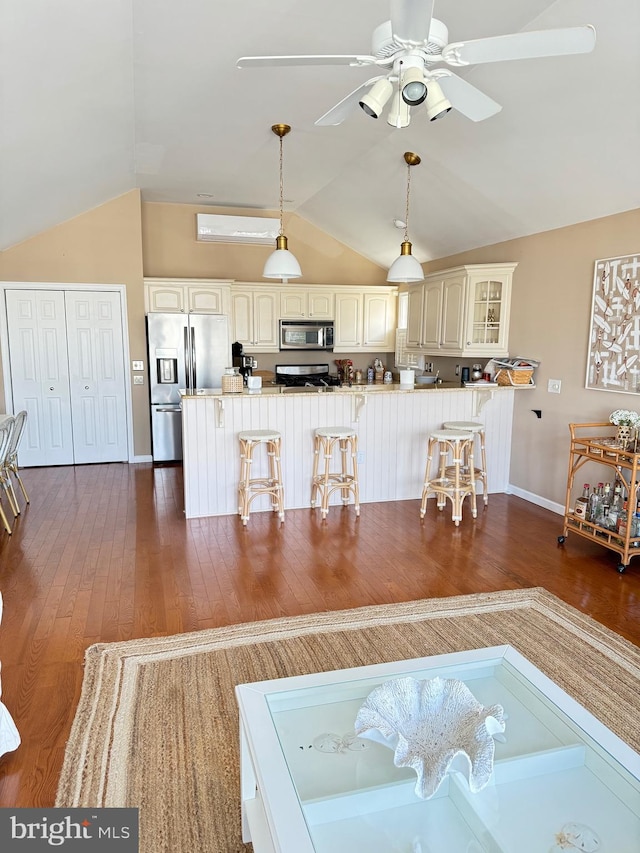 kitchen featuring stainless steel appliances, a breakfast bar, dark hardwood / wood-style flooring, vaulted ceiling, and decorative light fixtures