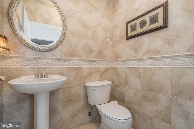 bathroom featuring toilet, tile walls, and sink