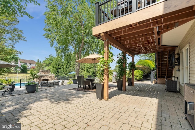 view of patio / terrace with an outdoor stone fireplace, a balcony, and a pool