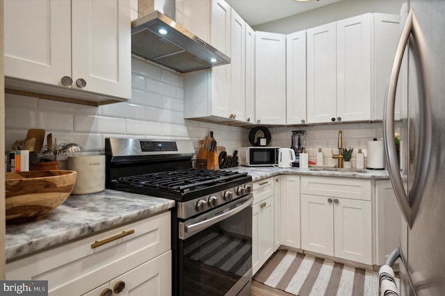 kitchen with wall chimney exhaust hood, tasteful backsplash, sink, appliances with stainless steel finishes, and white cabinetry