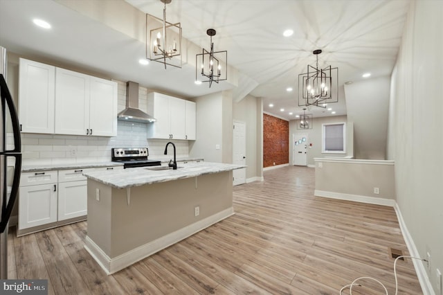 kitchen with wall chimney exhaust hood, pendant lighting, electric range, an island with sink, and white cabinetry