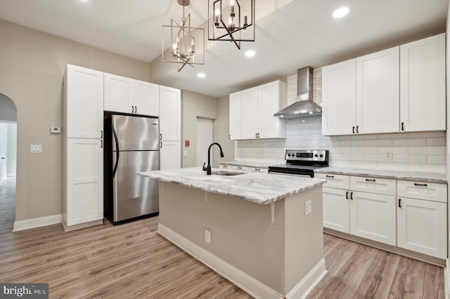 kitchen featuring sink, wall chimney exhaust hood, a kitchen island with sink, white cabinetry, and appliances with stainless steel finishes