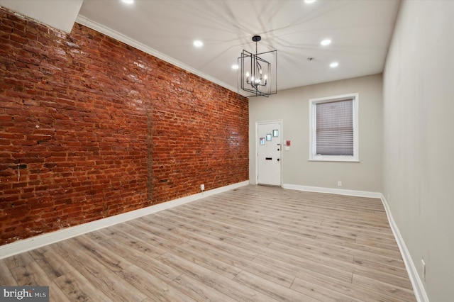 unfurnished dining area with an inviting chandelier, crown molding, light hardwood / wood-style flooring, and brick wall