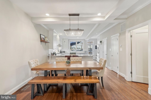 dining area with beam ceiling, light hardwood / wood-style floors, an inviting chandelier, and crown molding