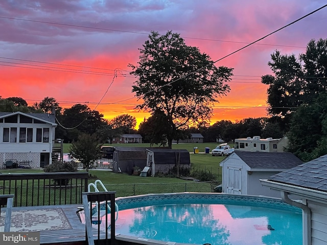 pool at dusk with a lawn, a sunroom, a shed, and a deck