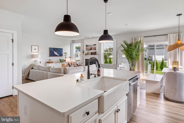 kitchen featuring a kitchen island with sink, sink, pendant lighting, white cabinetry, and light hardwood / wood-style flooring