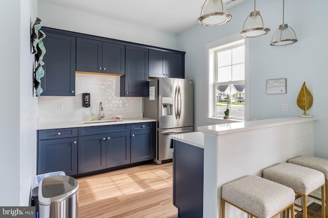 kitchen featuring light hardwood / wood-style floors, blue cabinetry, decorative light fixtures, sink, and stainless steel fridge with ice dispenser