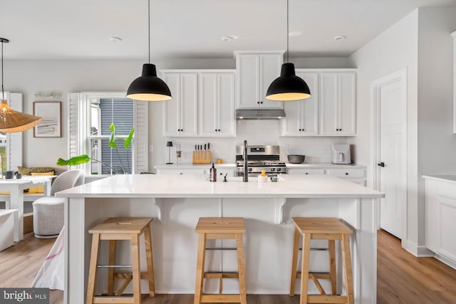 kitchen featuring a kitchen island with sink, gas range, white cabinetry, light hardwood / wood-style flooring, and backsplash