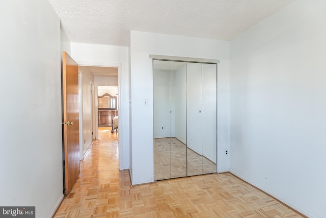 unfurnished bedroom featuring a closet, light parquet flooring, and a textured ceiling