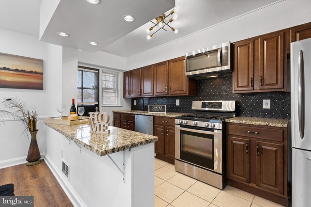 kitchen with backsplash, light stone countertops, light hardwood / wood-style floors, kitchen peninsula, and stainless steel appliances