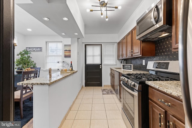 kitchen with backsplash, kitchen peninsula, light stone countertops, and appliances with stainless steel finishes