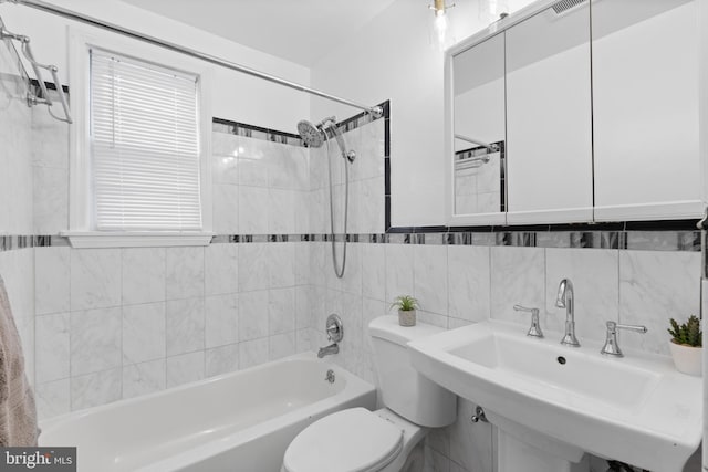 full bathroom featuring tiled shower / bath combo, toilet, sink, and tile walls