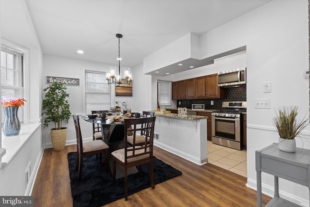 kitchen with kitchen peninsula, hardwood / wood-style floors, stainless steel appliances, and an inviting chandelier