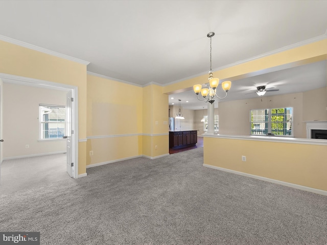 carpeted spare room featuring crown molding, a wealth of natural light, and ceiling fan with notable chandelier