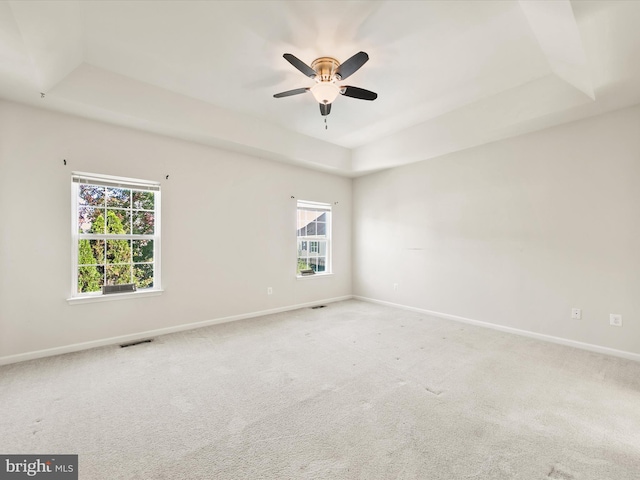 unfurnished room with ceiling fan, light colored carpet, and a raised ceiling